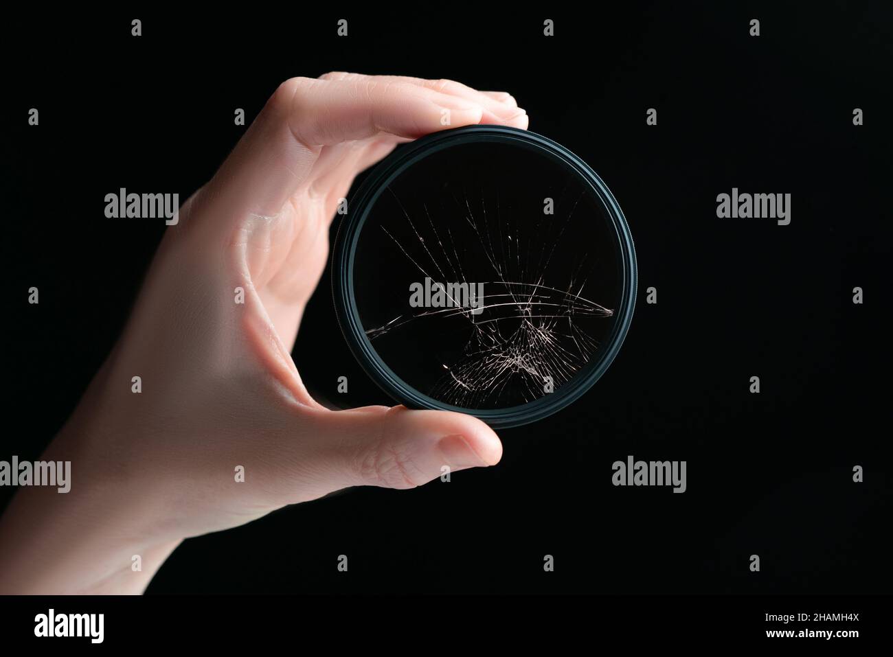 Nahaufnahme Studio Aufnahme der Hand hält schwarzen runden Polarisator-Filter mit gebrochenem Glas, isoliert auf schwarzem Hintergrund. Konzept für Schäden am Fotogetriebe Stockfoto