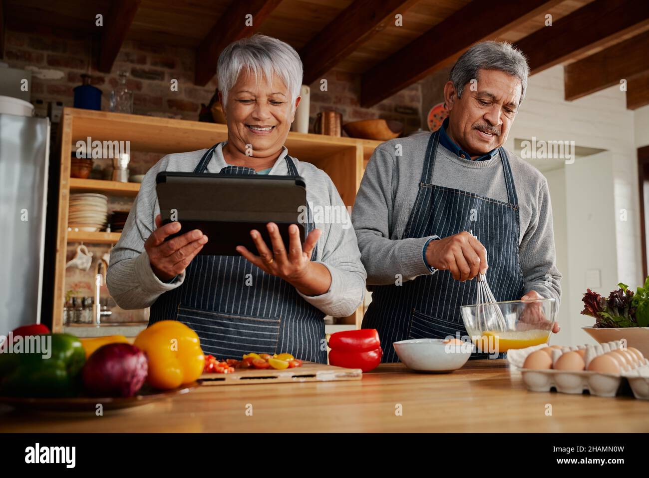 Hände von multikulturellen älteren Frauen, die ein Tablet benutzen, um Rezepte in der Küche zu erforschen. Glückliches Paar, das gesunde Mahlzeiten kocht. Stockfoto