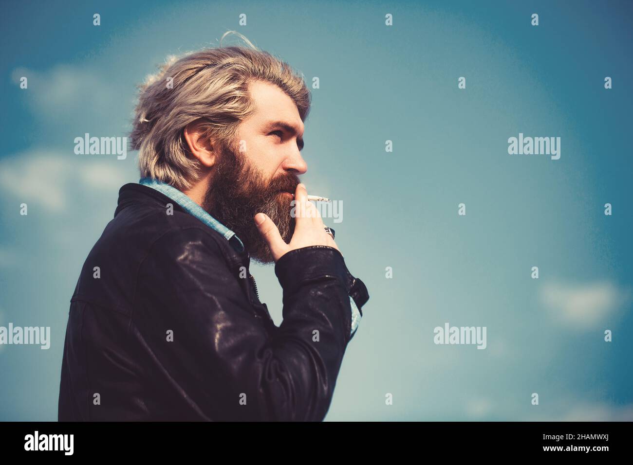 Das Gesicht eines Mannes mittleren Alters, der eine Zigarette raucht und nachdenklich aussieht. Vor blauem Himmel. Stockfoto