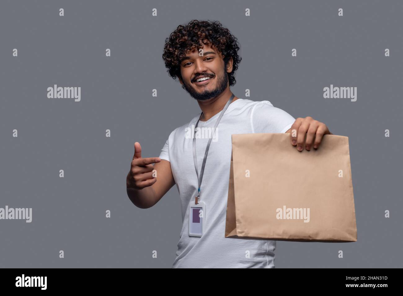 Lächelnder Deliveryman in einem T-Shirt mit einer Papiertüte Stockfoto