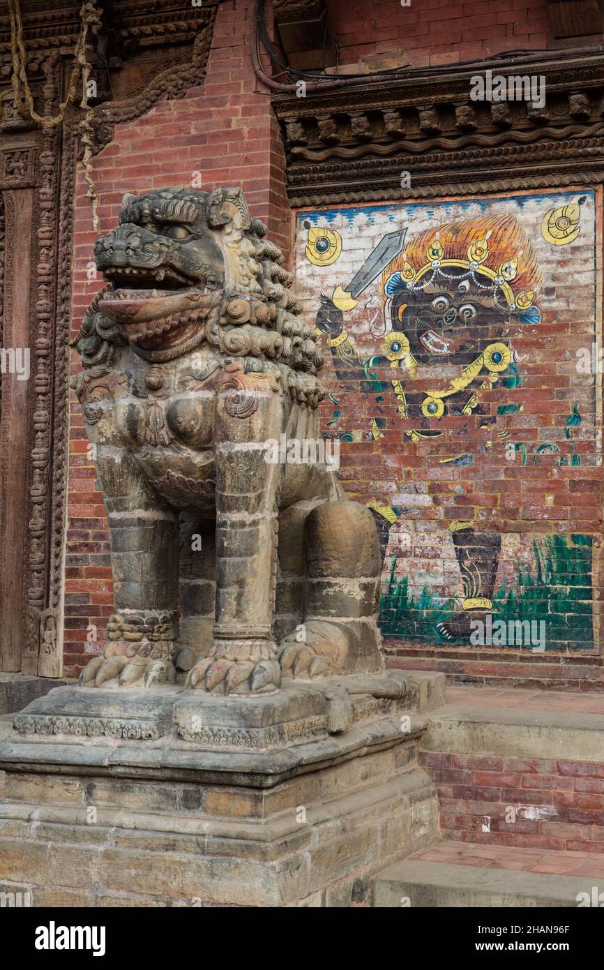 Ein steinerner Hüterlöwe vor dem alten königlichen Palast auf dem Durbar Square, Patan, Nepal. Dahinter ist ein Gemälde des Schwarzen Bhairabs. Stockfoto