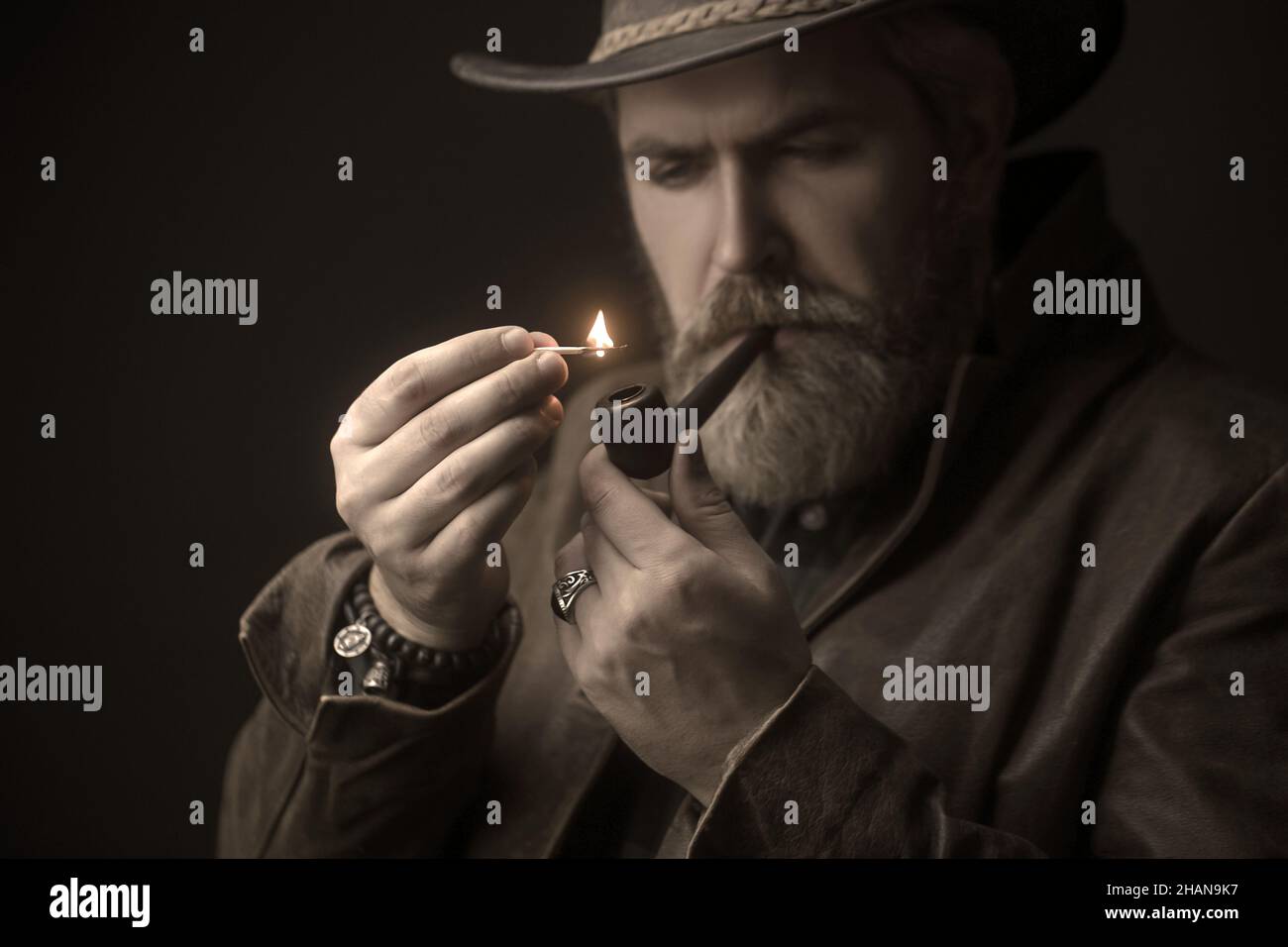 Bärtiger Mann, der Hut trägt und eine Pfeife raucht, sieht sehr ernst aus. Stockfoto