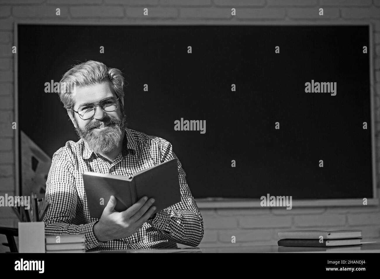 Fröhliche freundliche junge Lehrer oder Post-Graduate männlichen Schüler stehend Buch vor einem leeren Kreidetafel. Stockfoto