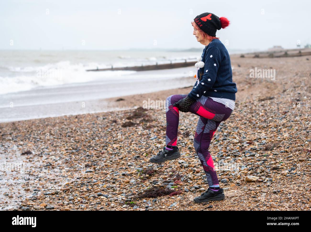 Ältere ältere Frau mit 80s Jahren an einem Strand am Meer, die im Winter trainiert. Alte Dame, die an der Südküste in Großbritannien einen aktiven und gesunden Lebensstil führt. Stockfoto