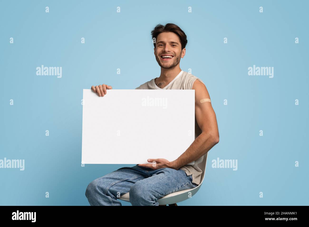 Impfkampagne. Junger Mann Mit Selbsthaftender Bandage Auf Leerem Schild Mit Armhalten Stockfoto