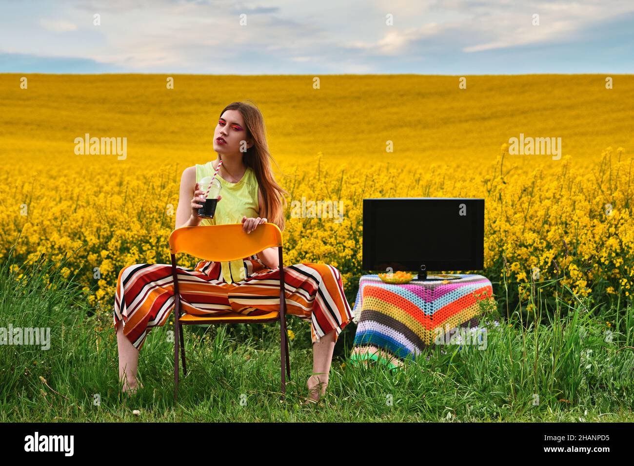 Mädchen sitzt auf einem Stuhl mit einem Getränk auf dem Feld Stockfoto