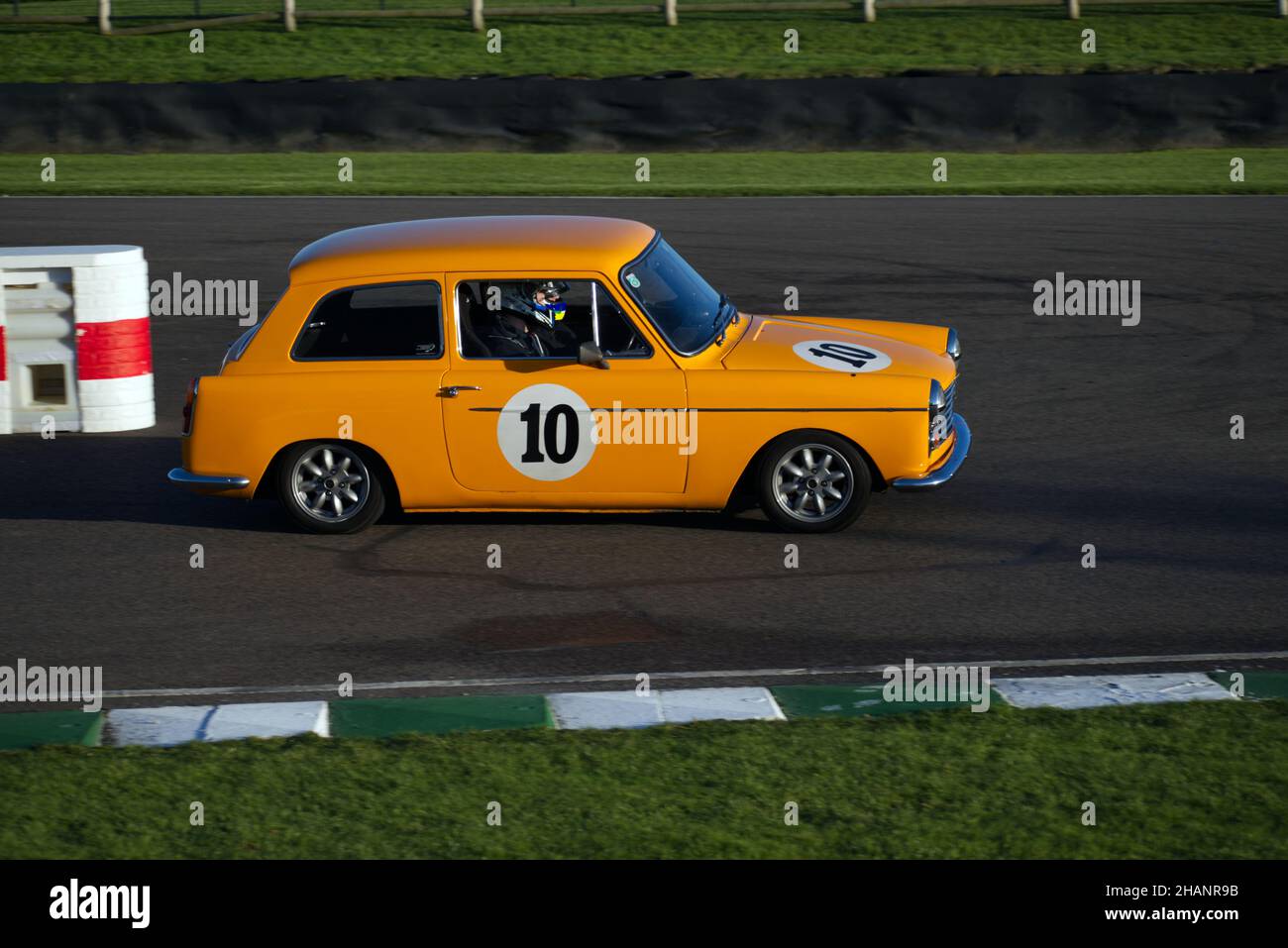 Ein gelber Klassiker Austin A40 im Renntrimm, der die Schikane verlässt und in die Zielgerade bei Goodwood eingeht. Stockfoto