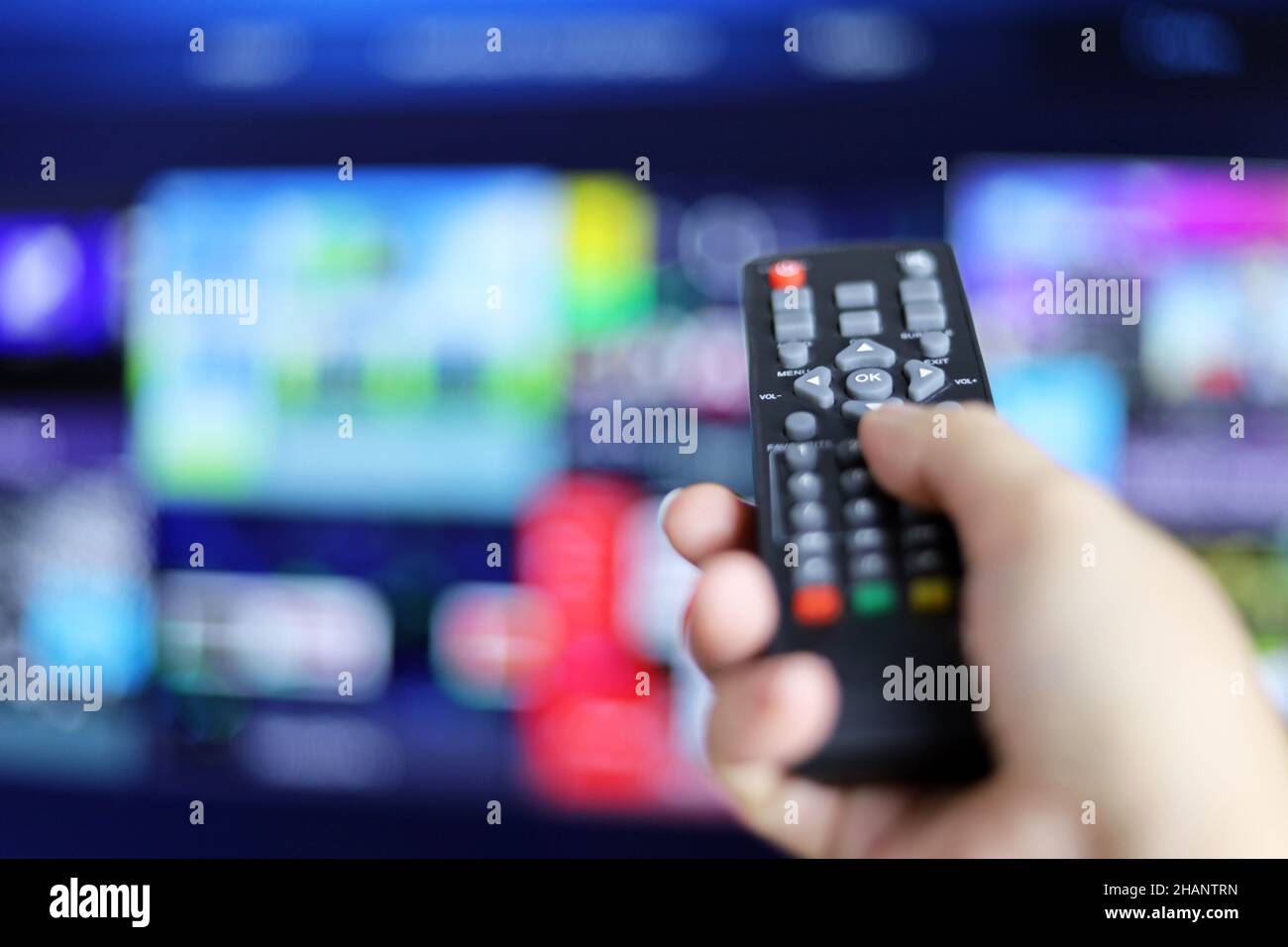 Fernbedienung in weiblicher Hand auf Smart TV-Bildschirm Hintergrund. Frau, die Streaming-Dienste wählt, Filme ansieht Stockfoto