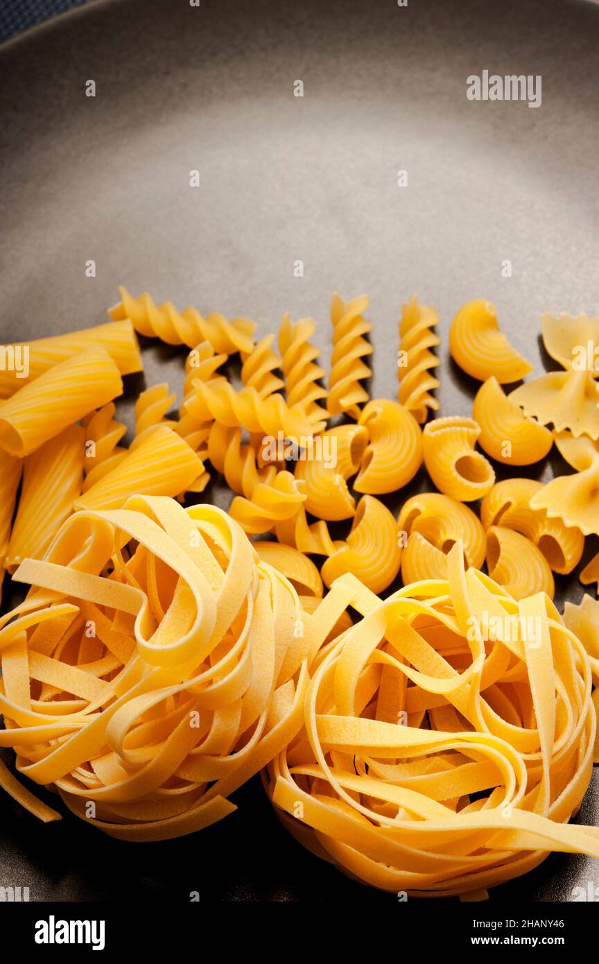 Verschiedene Arten von Pasta wie Fettuccine, Fusilli, Farfalle auf einem schwarzen Teller Stockfoto