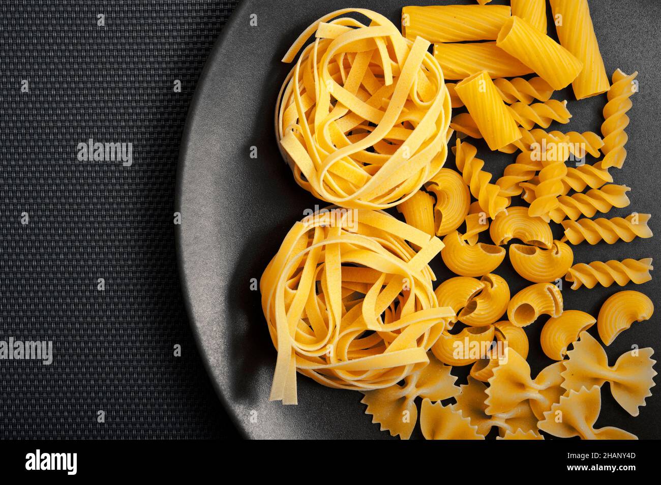 Verschiedene Arten von Pasta wie Fettuccine, Fusilli, Farfalle auf einem schwarzen Teller Stockfoto