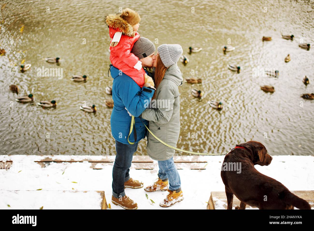 Familienportrait in voller Höhe mit einem Kind und Hund im Winter legeres  Outfit im Freien in Flussnähe mit Entenvögeln, Wochenendaktivitäten und  frischer Luft Stockfotografie - Alamy