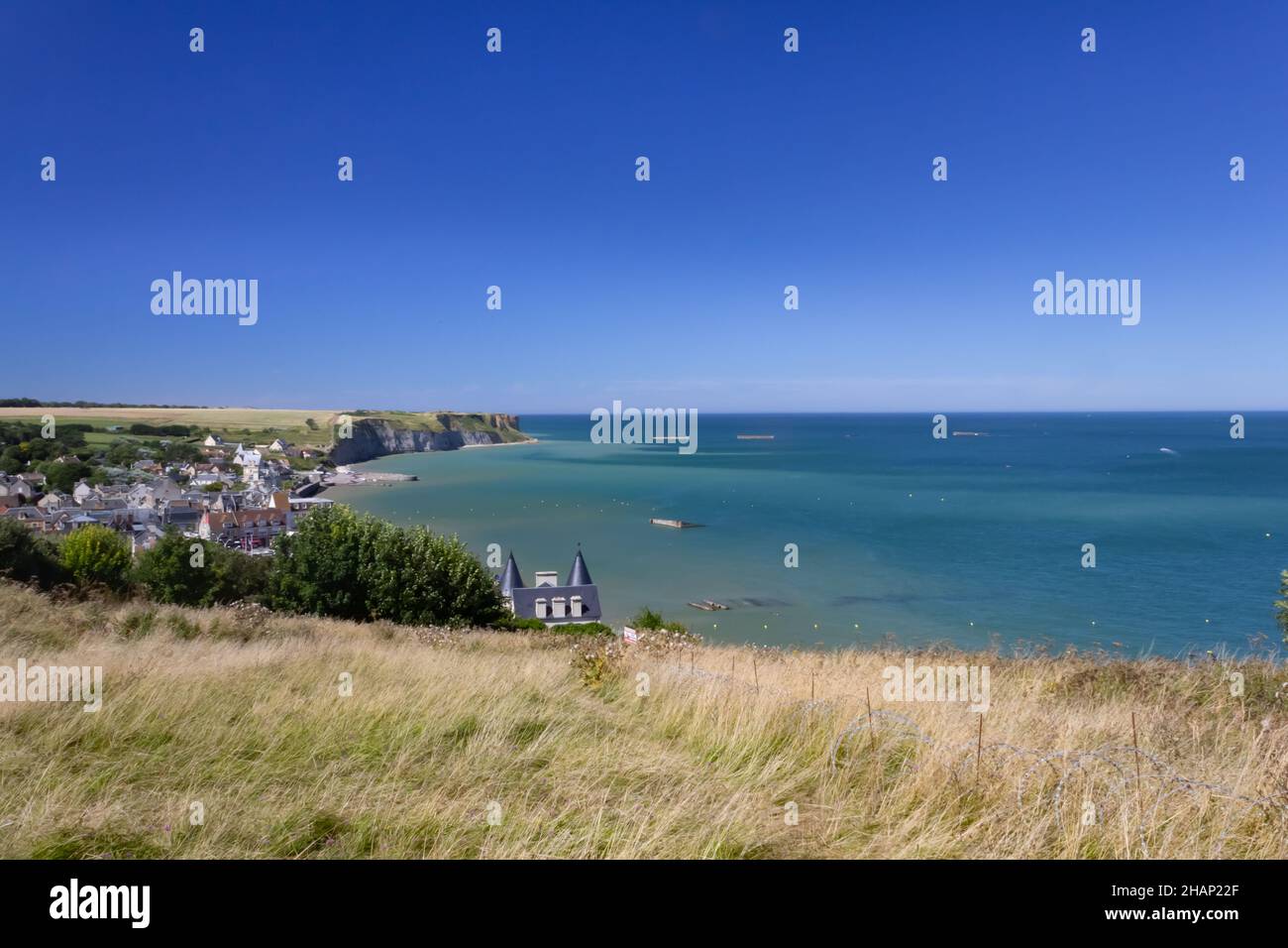 Blick auf die Bucht von Arromanches in der Normandie. Blauer Himmel und Wasser und sichtbare Überreste der Maulbeerbaumhafen Elemente des Weltkrieges. Stockfoto