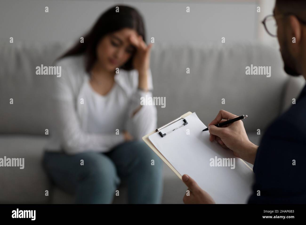 Deprimierte Frau aus dem Nahen Osten, die Psychologin im medizinischen Büro konsultiert, konzentriert sich auf das Schreiben eines Psychiaters in der Zwischenablage Stockfoto