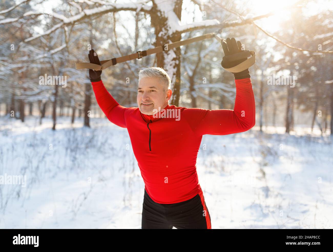 Sportlicher Senior, der an verschneiten Wintertagen mit TRX-Fitnessbändern im Freien trainiert Stockfoto