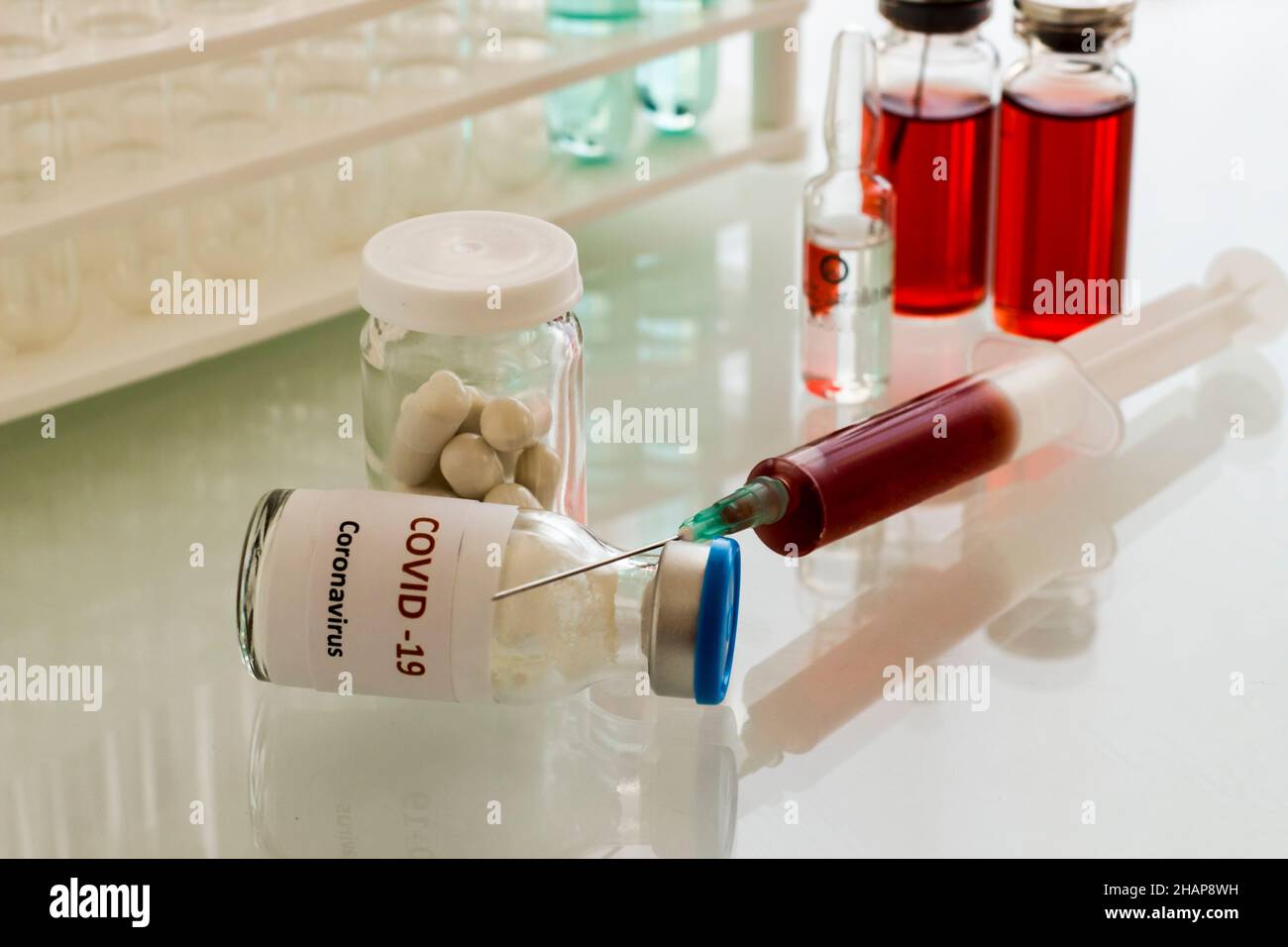 Mini-Medizinglas-Flasche und Injektor mit medizinischen Materialien auf dem Glastisch.Covid-19 ist auf der Flasche geschrieben Impfstoffarbeiten im Labor. Stockfoto