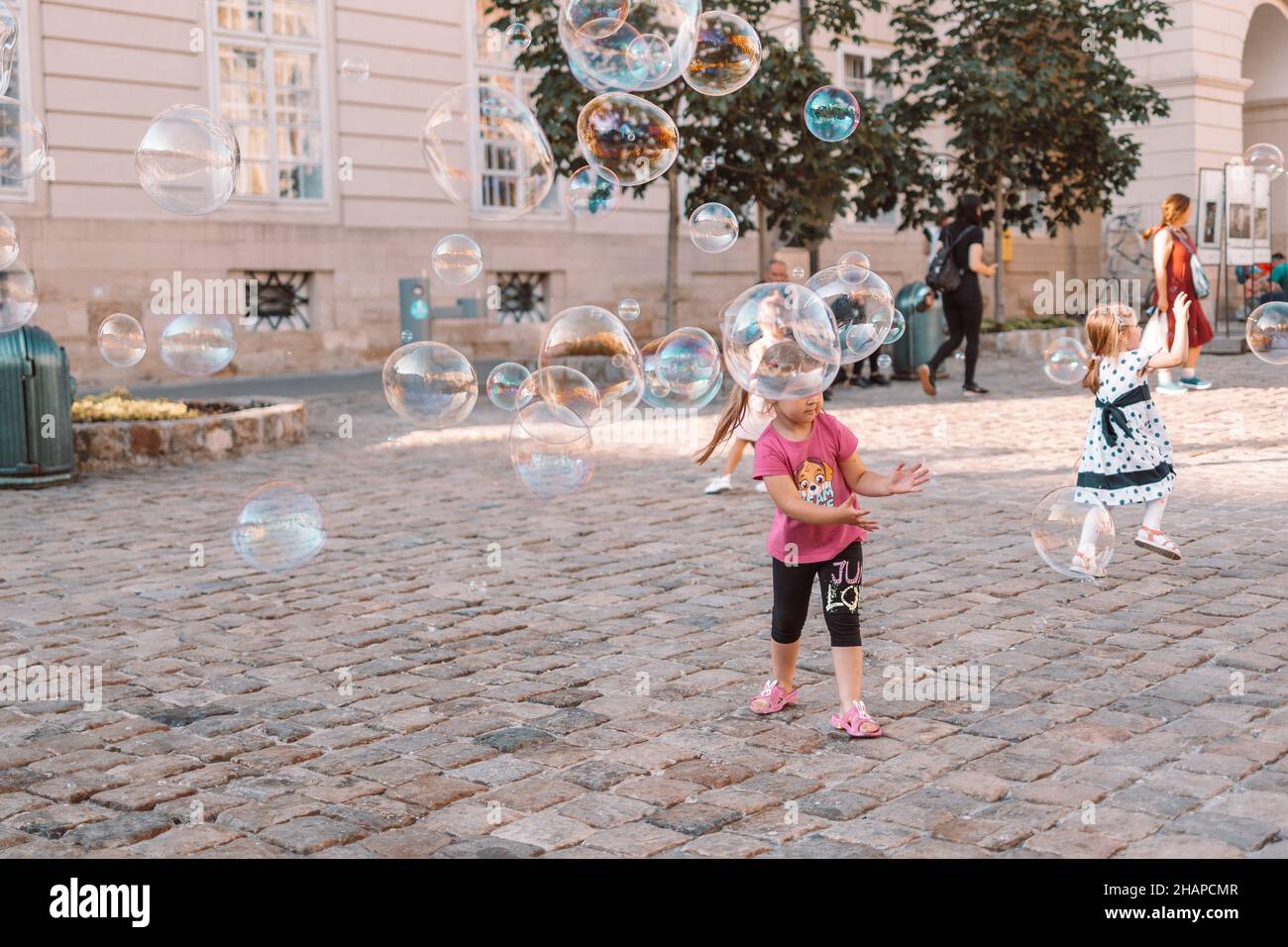 Große Seifenblasen fliegen draußen in die Luft. Kinder spielen im Hintergrund am Sommertag Stockfoto