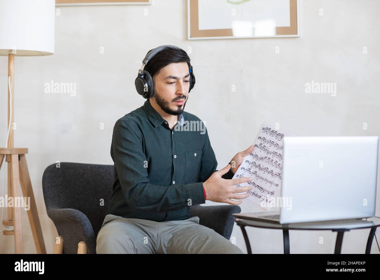 Junge Musiklehrerin in Kopfhörern, die Noten mit Noten zeigt, während sie mit dem Online-Publikum kommuniziert Stockfoto