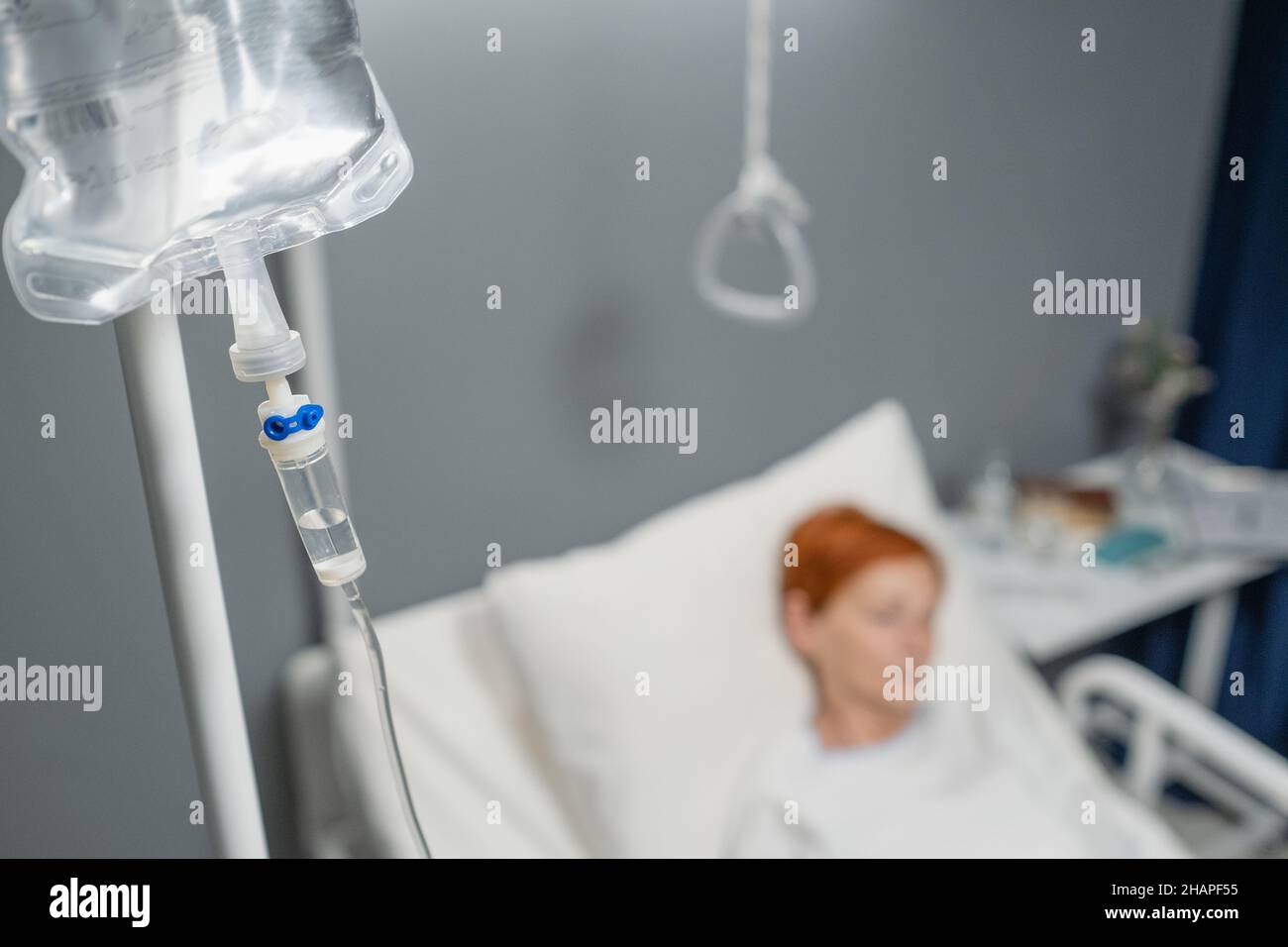 Nahaufnahme eines infusionstropfes über dem Bett mit einer älteren Frau, die nach der Operation auf der Krankenstation schlief Stockfoto