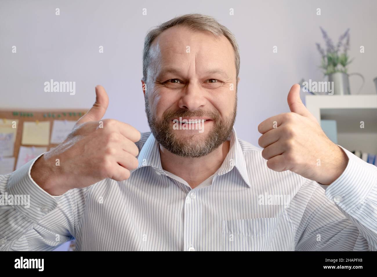 Mann mittleren Alters zeigt Daumen nach oben in homa Büro. Online-Anrufkonzept Stockfoto