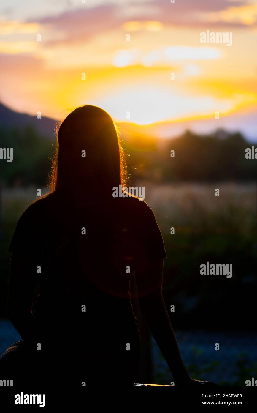 Silhouette eines jungen Teenagers, das auf der Bank sitzt Stockfoto