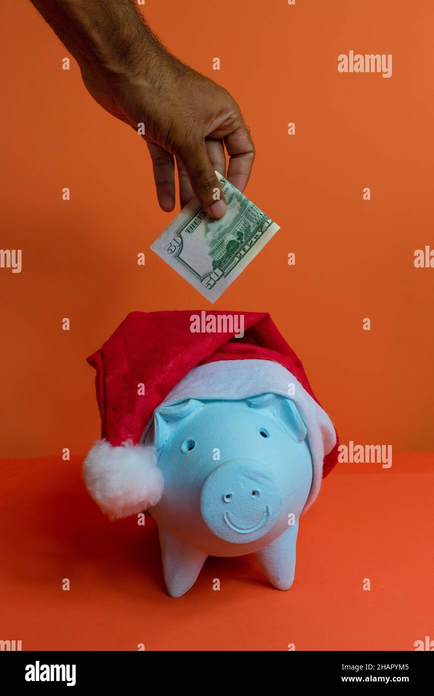 Hand setzen Dollar Geld in Sparschwein mit weihnachtsmann Hut isoliert auf orangefarbenem Hintergrund. Stockfoto