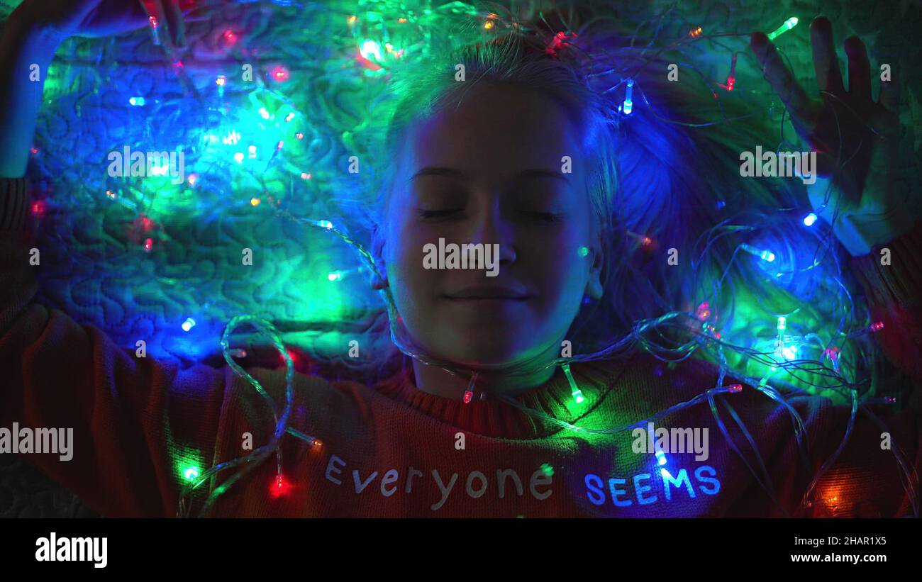 Blonde Teenager Mädchen liegt in Girlande Lichter für weihnachten, zeigt Herz mit einem Brüllen und lächelt. Stockfoto