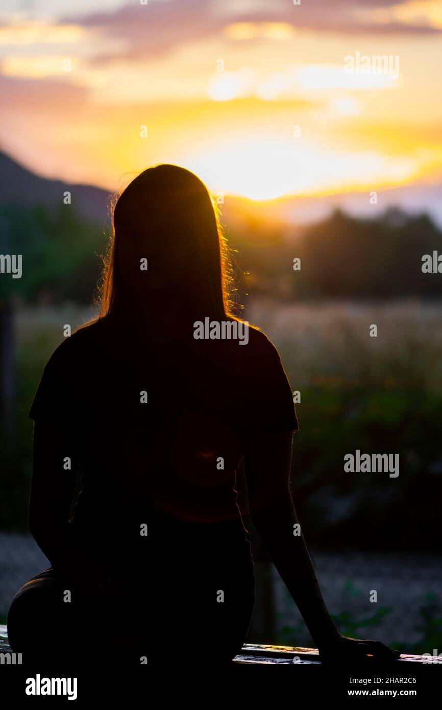 Silhouette eines jungen Teenagers, das auf der Bank sitzt Stockfoto
