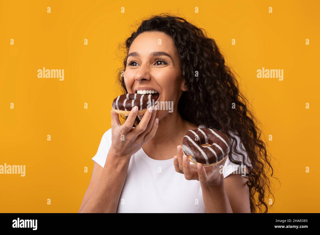 Happy Latin Lady Holding Donuts Beißen Kuchen Im Studio Stockfoto