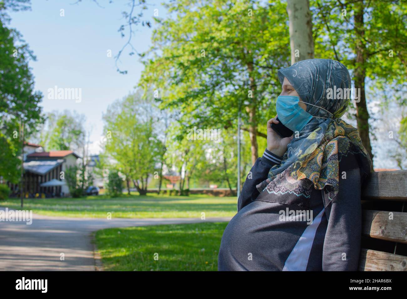 Profilansicht der muslimischen Schwangeren, die eine Gesichtsmaske tragen und auf dem Smartphone sprechen Stockfoto