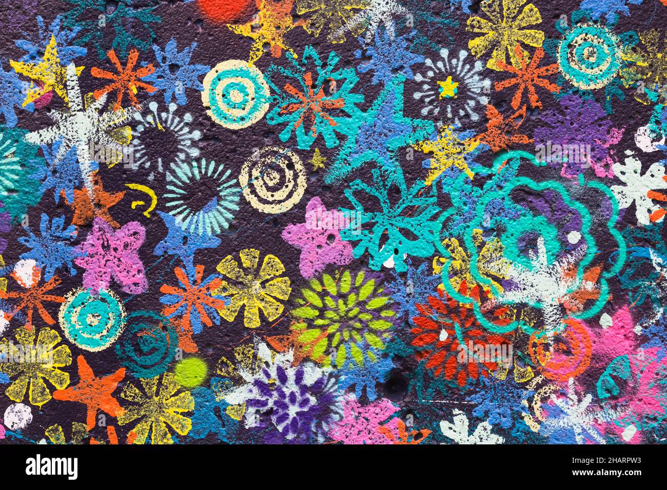 Bunt bemalte Blumenmuster auf dunkelblauer Betonwand. Stockfoto