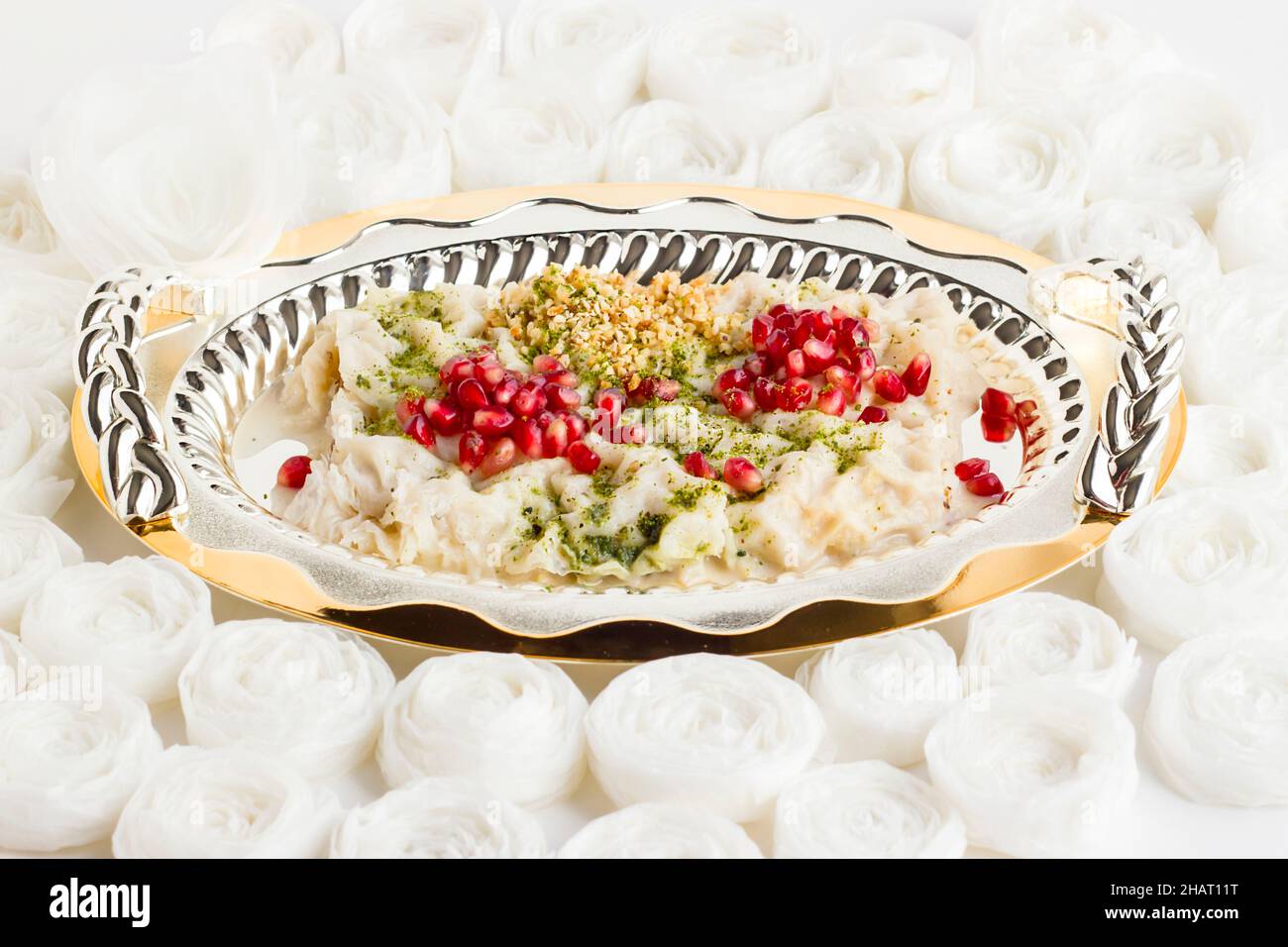 Von der osmanischen Küche bis zur türkischen Küche ein traditionelles Dessert Gulac, in stilvollem, glänzendem Metall, Tablett auf handgefertigten Papierrosen. Stockfoto