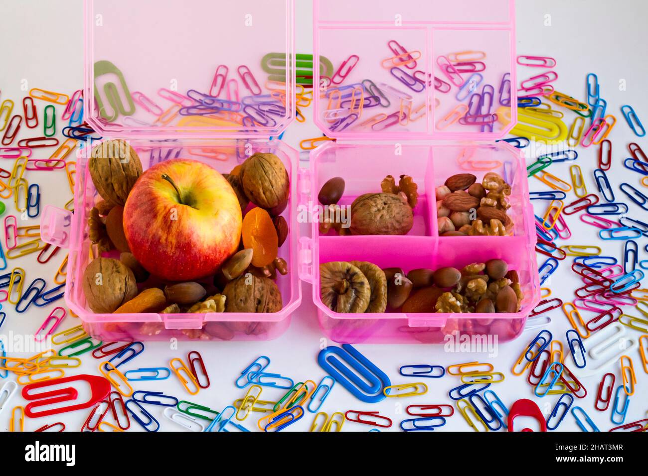 Rosa, harte Kunststoff-Lebensmittelbox für Schulkinder auf bunten Büroklammern entworfen.Apfel, trockene Früchte und gemischte Nüsse. Stockfoto