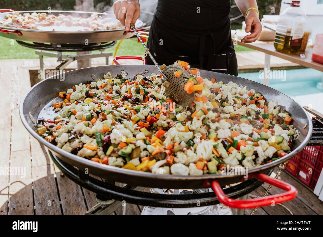 Prozess der Zubereitung von Paella in einer Pfanne mit Huhn und Gemüse und Köchin's Hand würzen und Kochen auf einer Terrasse in Spanien Stockfoto