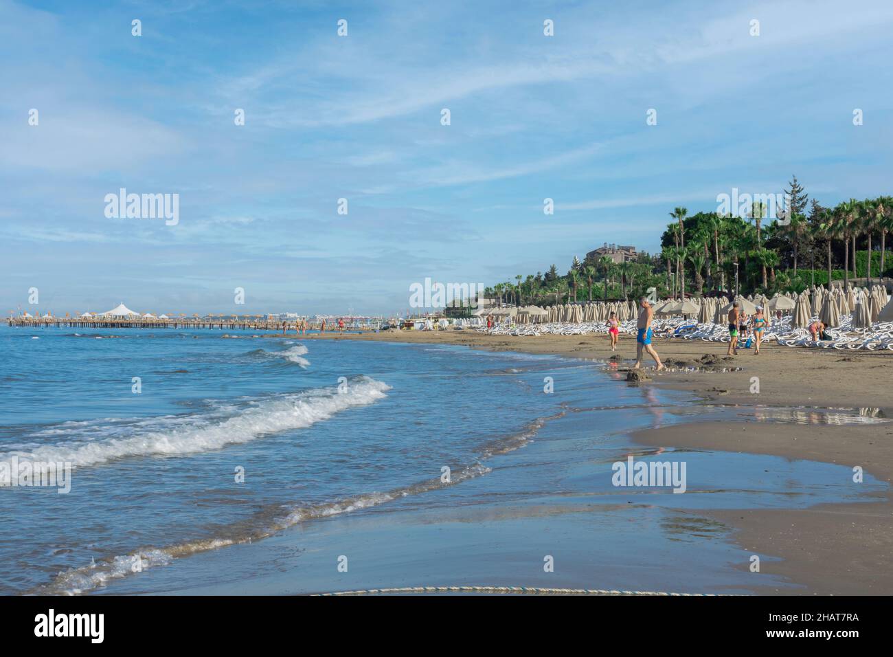 Blick auf den Strand, Liegestühle, Sonnenschirme, Flaggen und kleine wellige Küste in Antalya Seite. Selektiver Fokus. Stockfoto