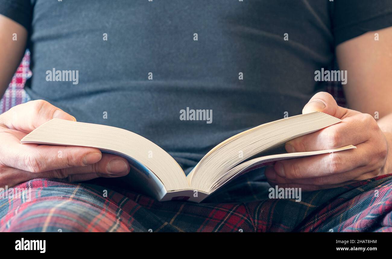 Mann, der zu Hause ein Buch liest und umdreht. Nahaufnahme einer Person Hände mit einem geöffneten weißen Buch. Stockfoto