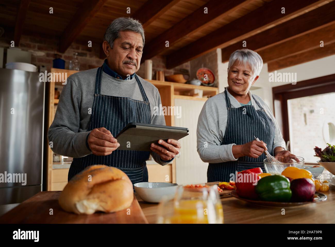 Multikulturelles älteres Paar nach Rezept auf elektronischer Tablette, um gesunde Mahlzeiten in der modernen Küche zu kochen. Stockfoto