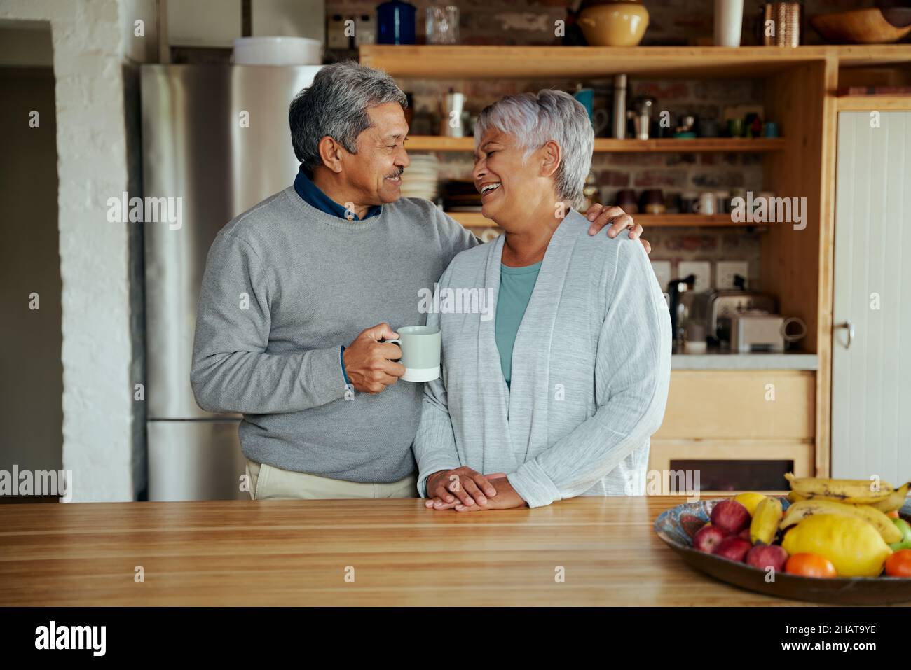 Liebevolles Senioren-Biracial-Paar im Ruhestand, das sich gegenseitig anlacht, während es in der modernen Küche steht. Stockfoto