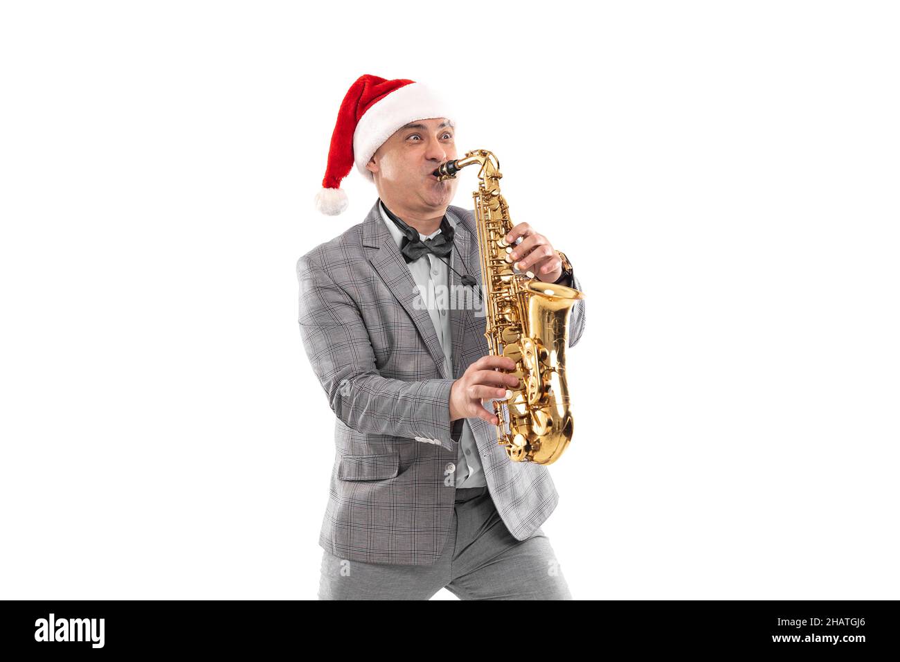 Eleganter erwachsener Mann trägt in Santa's Hut spielt auf Saxophon auf weißem Hintergrund. Silvesterparty Stockfoto