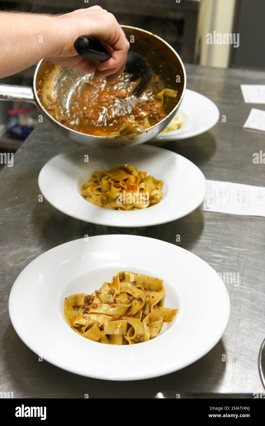 Von oben der Ernte anonymen Koch Putting appetitlich freche Tagliatelle Pasta aus der Pfanne in Keramikplatten auf dem Tisch in der Restaurantküche platziert Stockfoto