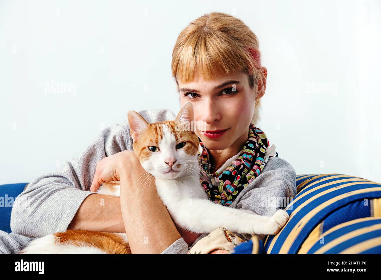 Inhalt Ingwer-Weibchen sitzt auf der Couch und umarmt weiße und rote Katze, während sie auf die Kamera schaut Stockfoto