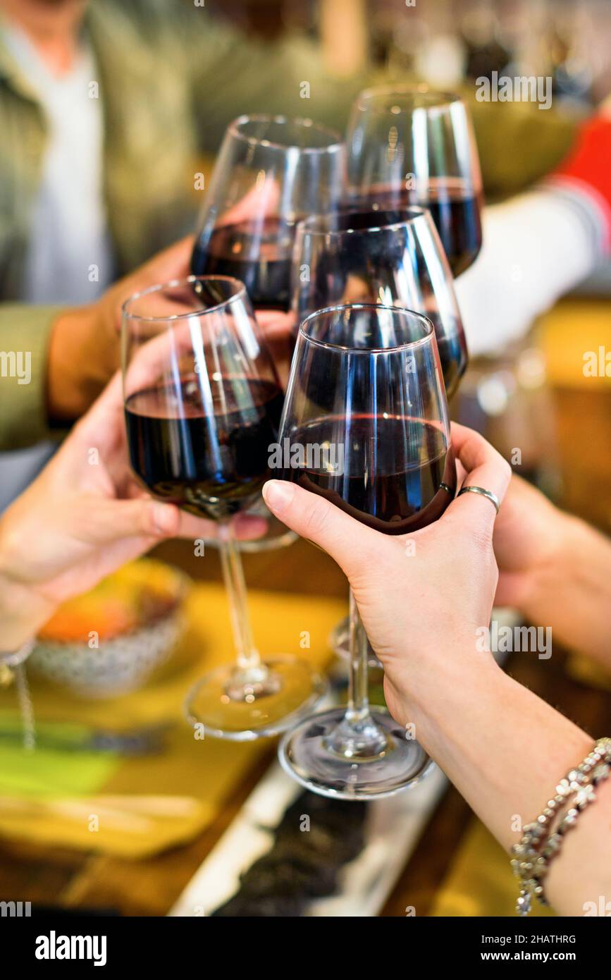 Schneiden Sie eine anonyme Gruppe von Freunden, die in einem hellen, modernen Restaurant mit Rotwein klirren, während Sie gemeinsam eine festliche Veranstaltung am Tisch feiern Stockfoto