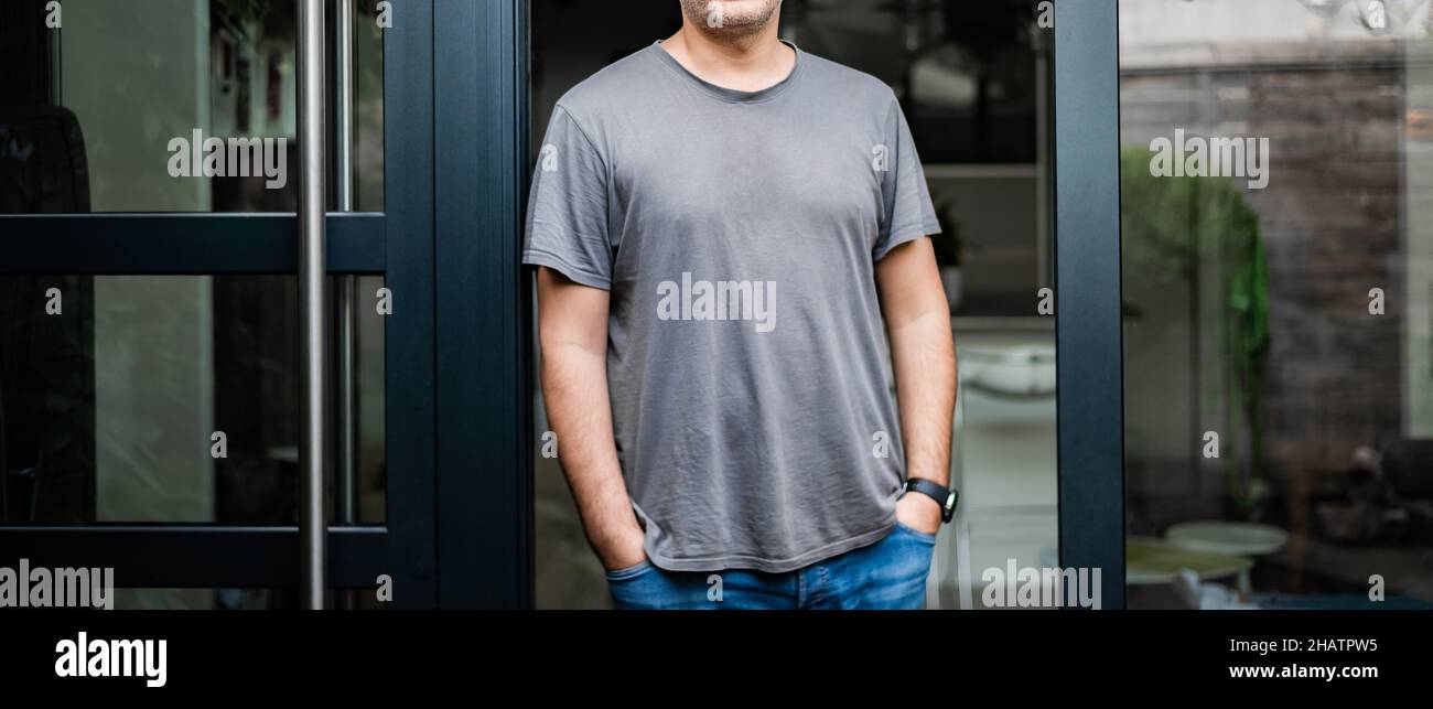 Aufnahme eines gesichtslosen Mannes mit dem mittleren Körperteil oder eines sorglosen, zwanglosen Geschäftsmannes, der vor der Haustür seines Heims oder Heimbüros steht. Grau real life blank t-sh Stockfoto