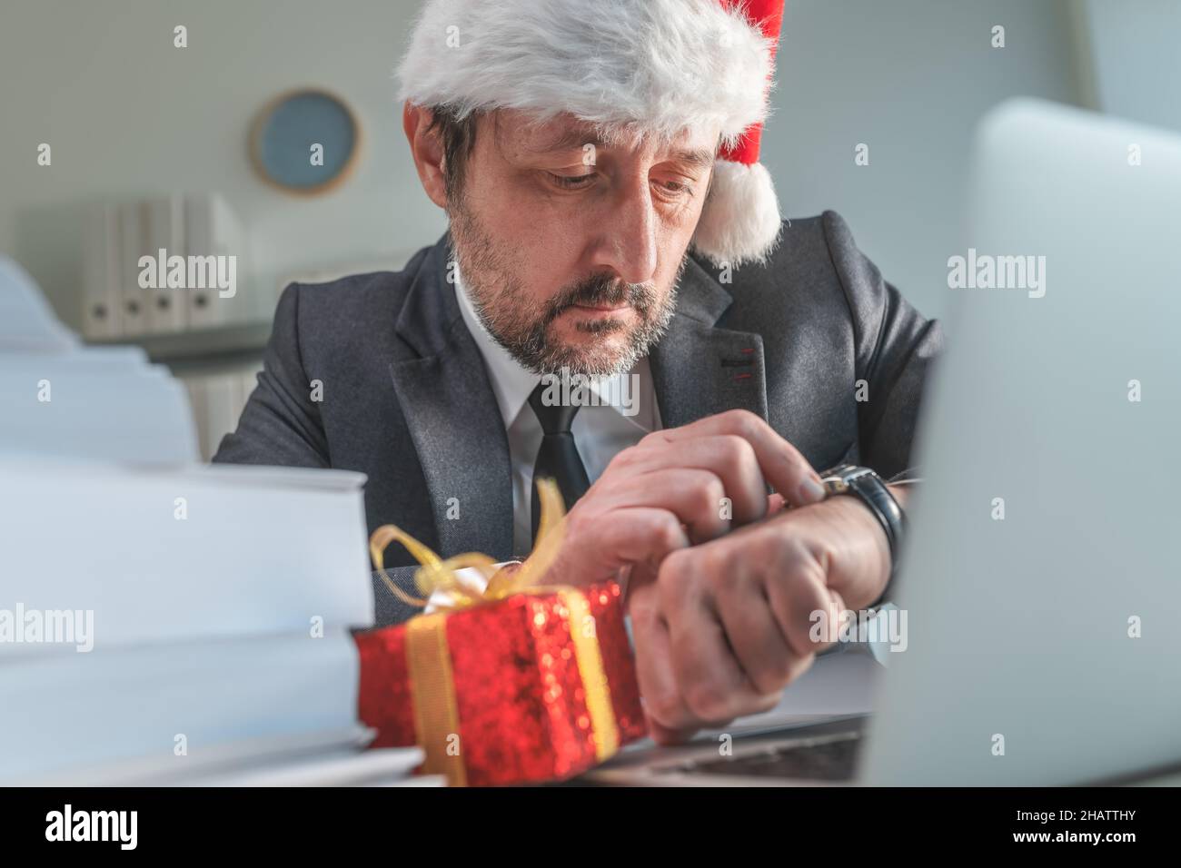 Nervöser Geschäftsmann mit Weihnachtsmannhut, der während der Weihnachtsfeiertage die Zeit auf seiner Uhr überprüft, selektiver Fokus Stockfoto
