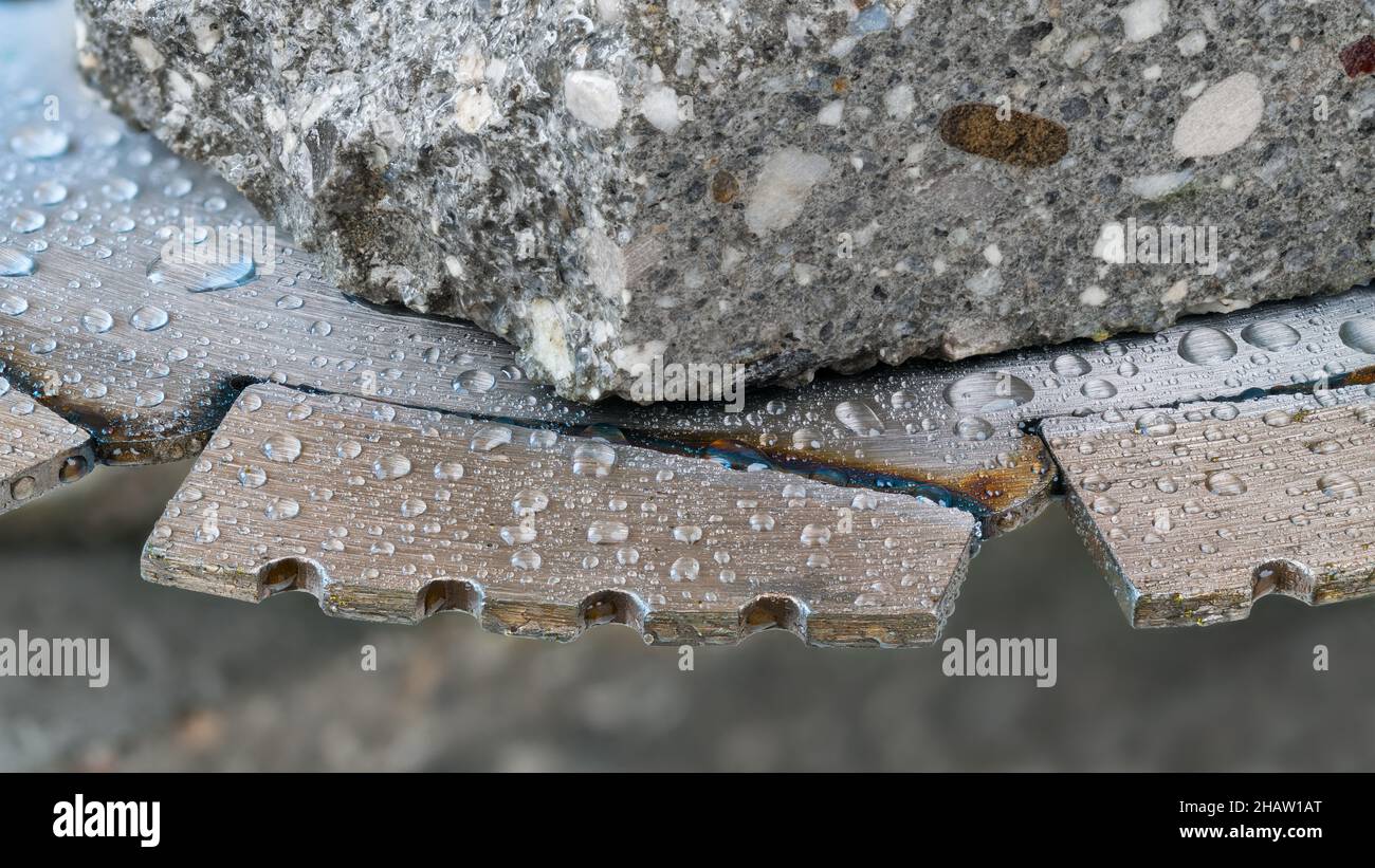 Nahaufnahme der Diamantsegmente des Sägeblatts mit Wassertropfen und einem Stück einer grauen Fliese. Scharfe Schneidscheibe aus Stahl des Elektrowerkzeugs zum Nassschneiden von Beton, Ziegel. Stockfoto