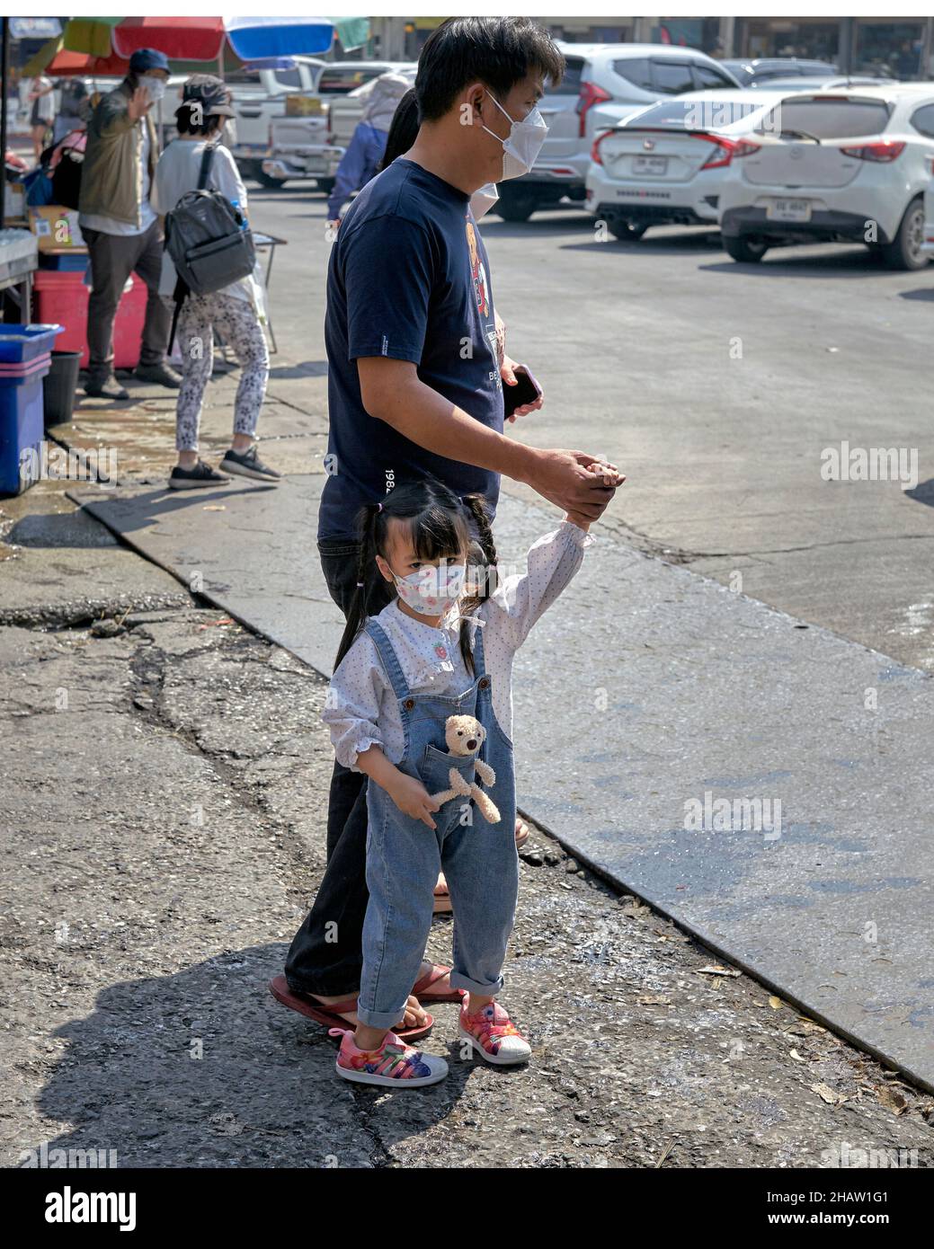 Das Kind trägt ihren Teddybären in einer Tasche vorne, während es draußen mit ihrem Vater unterwegs ist Stockfoto