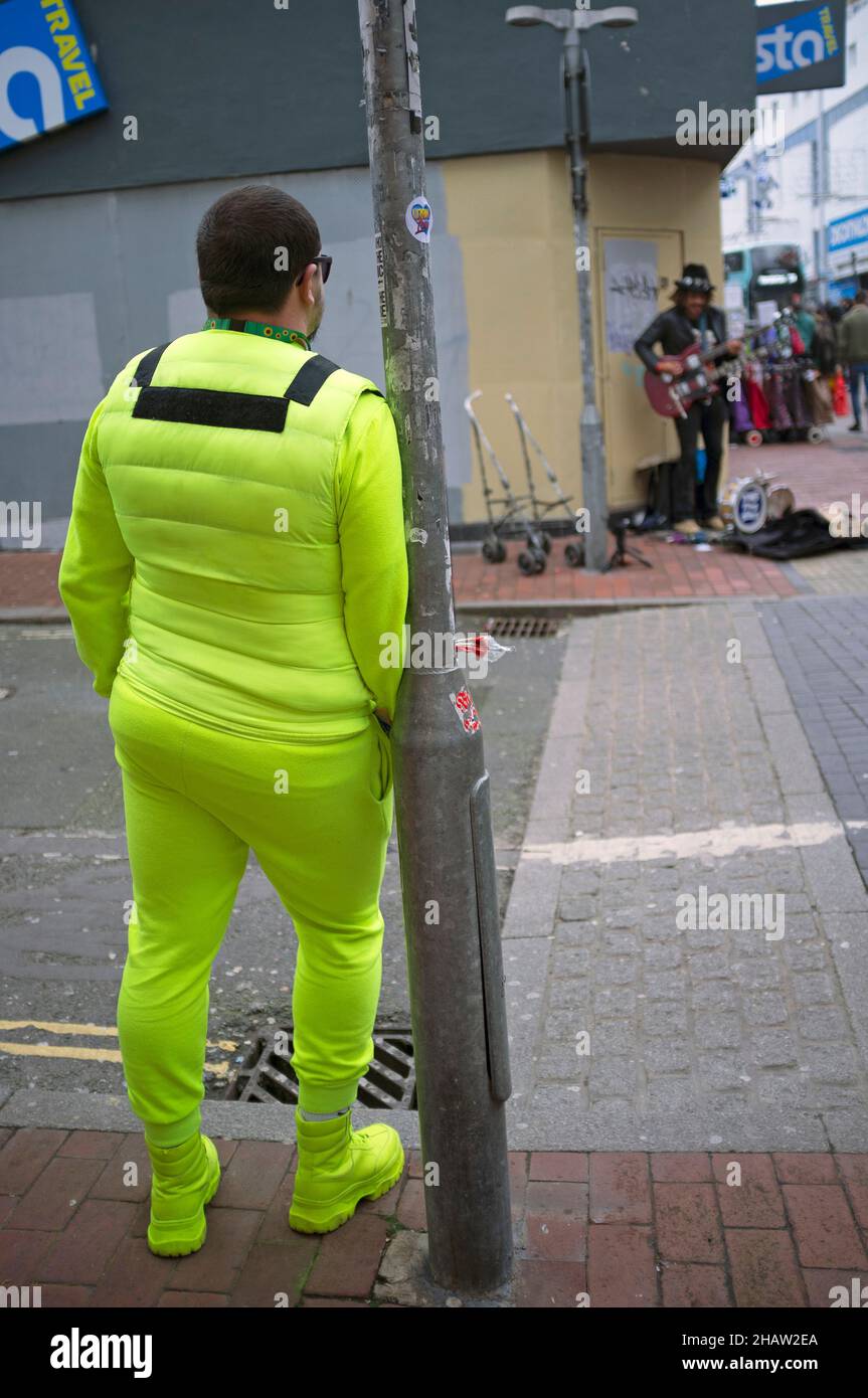 Ein Mann in einem gelben Trainingsanzug wartet an einer Straßenecke in Brighton Stockfoto
