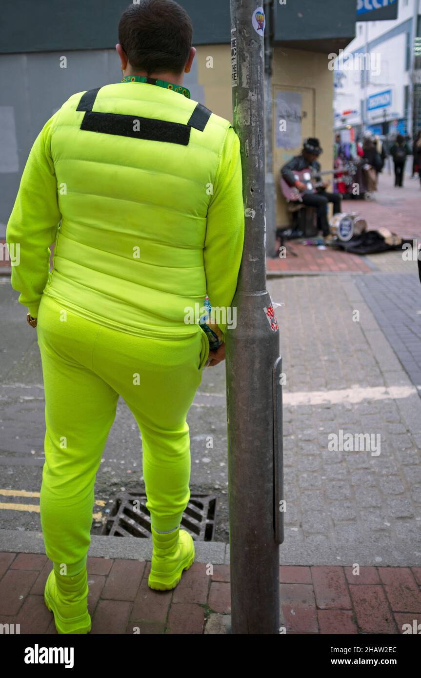 Ein Mann in einem gelben Trainingsanzug wartet an einer Straßenecke in Brighton Stockfoto