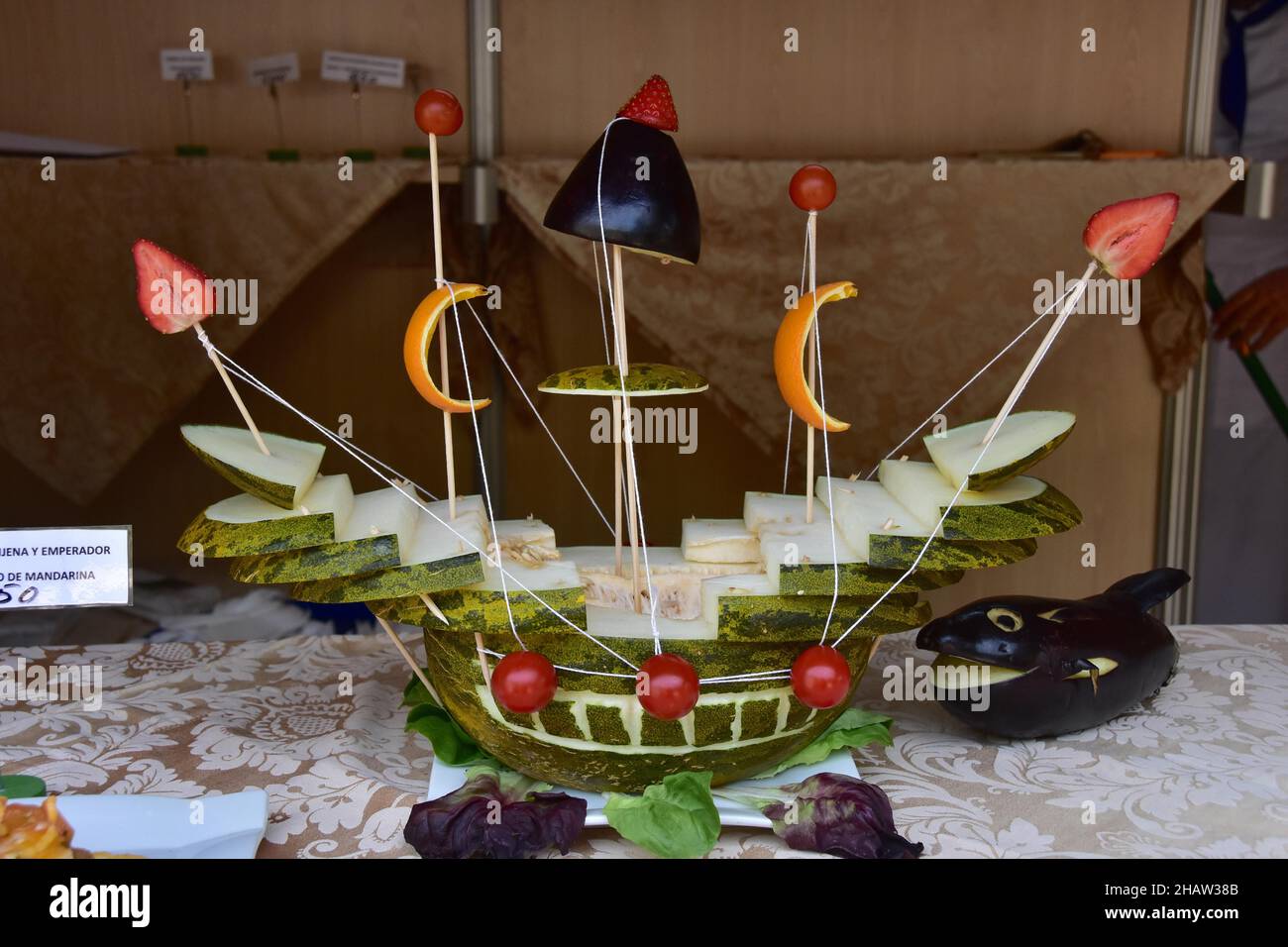 Dekoriertes Obst- und Gemüseschiff, Schiff mit Obst und Gemüse, Aubergine, Wassermelone, Erdbeere, Orangenschale, Salatblätter, Tischdekoration Stockfotografie