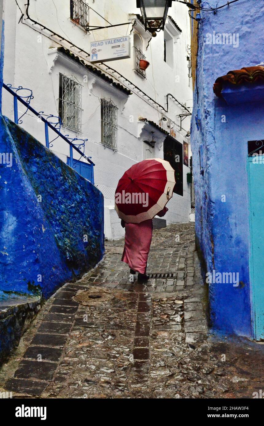 Frau mit rotem Regenschirm in den Gassen von Chefchaouen, weibliche Schirmträger in Nieselregen, Blue City, Chefchaouen, Tanger-Tetouan-Al Hoceima, Marokko Stockfoto