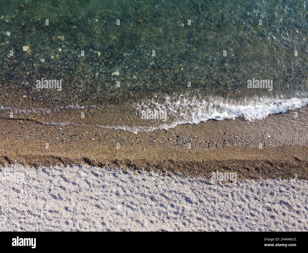 Luftaufnahme von oben auf ruhiges azurblaues Meer und Kiesstrand. Kleine Wellen auf kristallklarem Wasser verschwimmen in Bewegung. Sommer Meer Meer Strand Stockfoto
